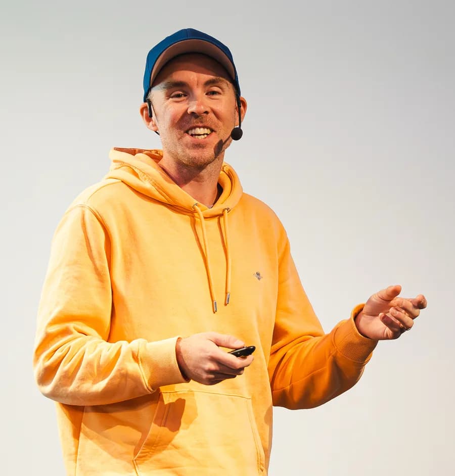 Sibbe Silvén föreläser i gul hoodie och blå keps, med headset och presenter i handen