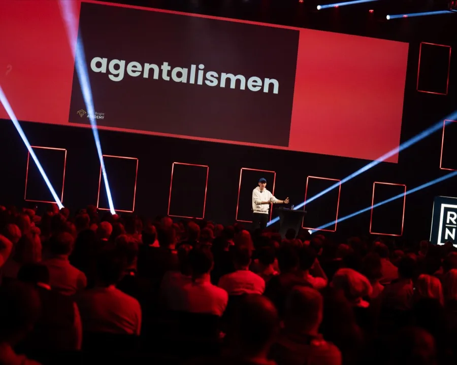 Visa större: Sibbe Silvén på scen framför fullsatt salong med presentationen Agentalismen på storbildsskärmen